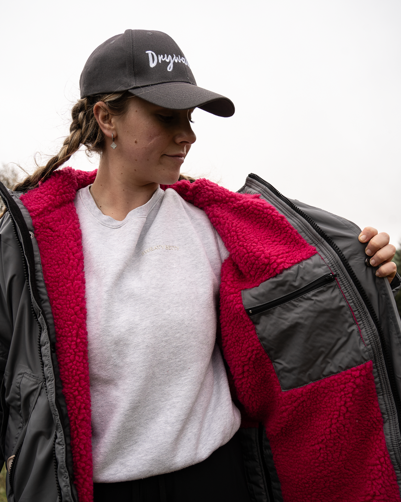 Person wearing a grey & pink long oversized Drywalks coat with a black Drywalks cap.